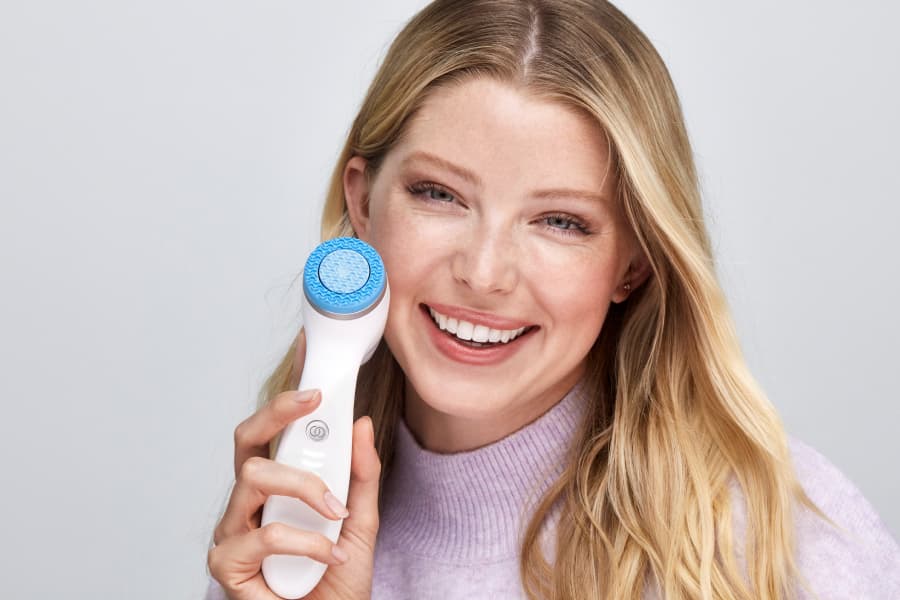 Woman holding the ageLOC LumiSpa iO device to her cheek, smiling